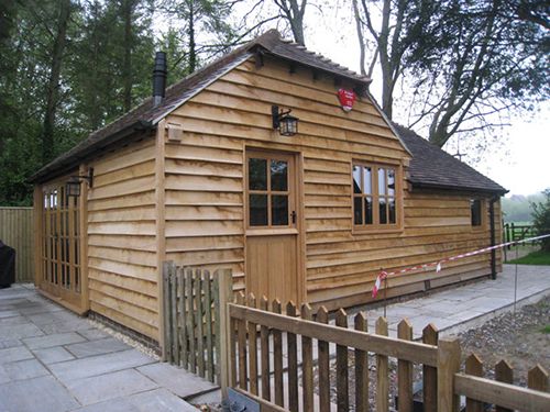 Timber-clad garden building with a picket fence and paved patio