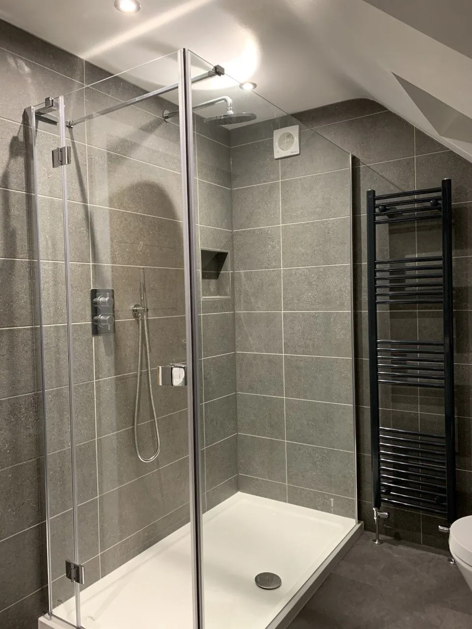 Walk-in glass shower with grey tiles and a towel radiator