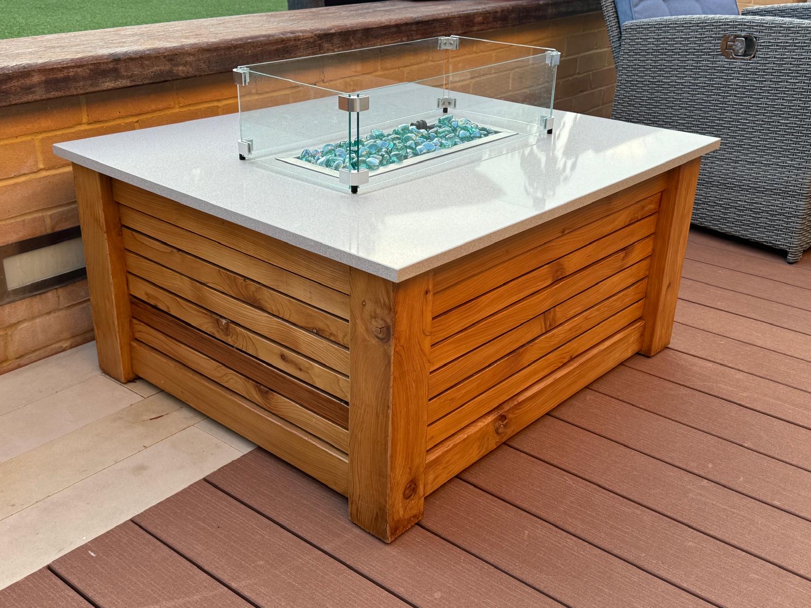 Modern rectangular gas fire pit table with glowing blue glass fire stones on a contemporary patio.